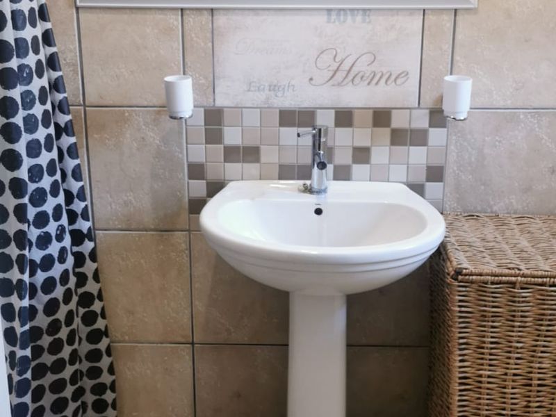 A functional bathroom featuring a pedestal basin with chrome mixer tap, tiled splashback, and a wall-mounted mirror.