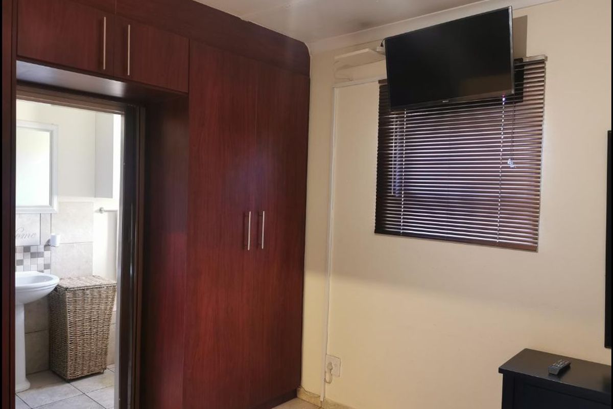 A bedroom featuring dark wood built-in cupboards, venetian blinds, and an adjoining bathroom with tiled finishes.