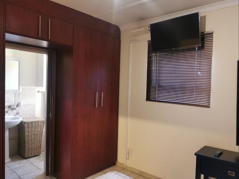 A bedroom featuring dark wood built-in cupboards, venetian blinds, and an adjoining bathroom with tiled finishes.