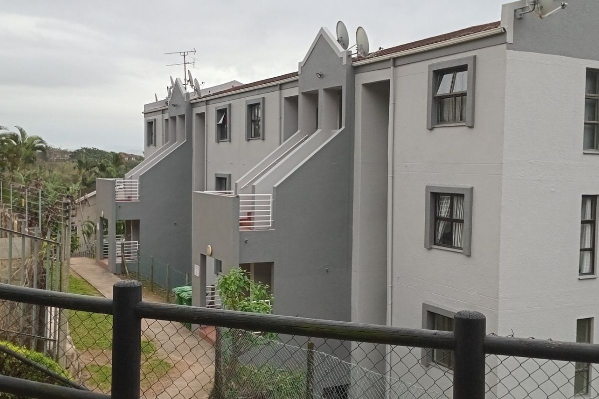 Rear view of a multi-story apartment complex featuring grey and white facade, private balconies, and a paved walkway.