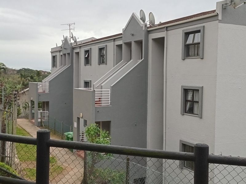 Rear view of a multi-story apartment complex featuring grey and white facade, private balconies, and a paved walkway.
