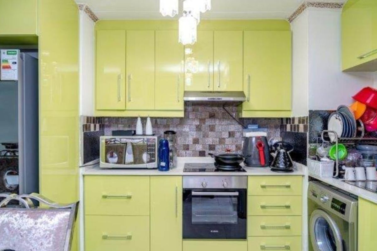 A compact kitchen featuring lime green high-gloss cabinetry, a mosaic tile backsplash, built-in oven, hob, extractor fan, and an integrated washing machine.