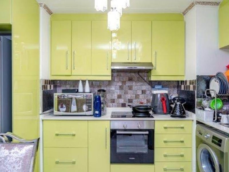 A compact kitchen featuring lime green high-gloss cabinetry, a mosaic tile backsplash, built-in oven, hob, extractor fan, and an integrated washing machine.
