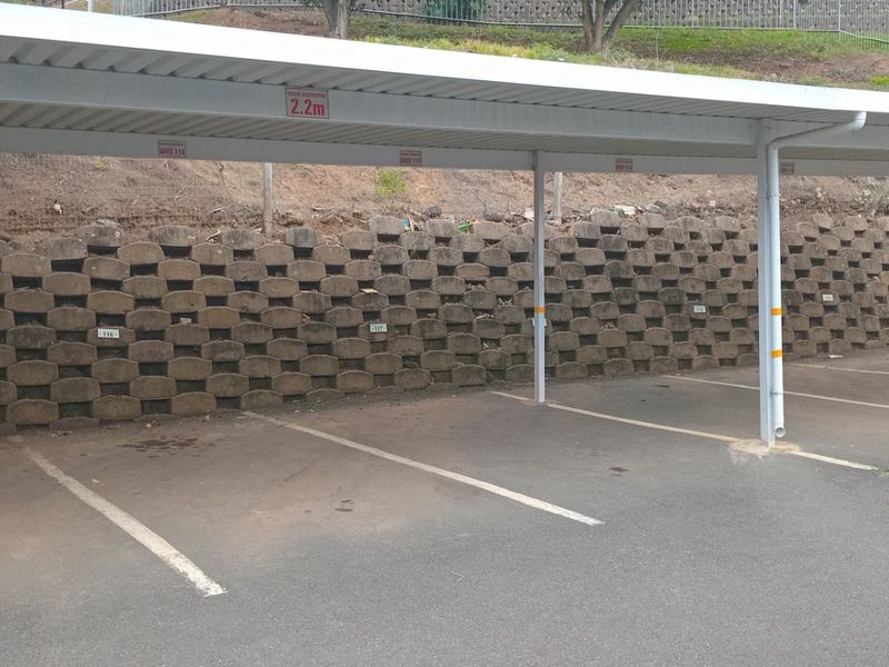 A covered parking area featuring multiple designated bays, asphalt paving, and a concrete block retaining wall.