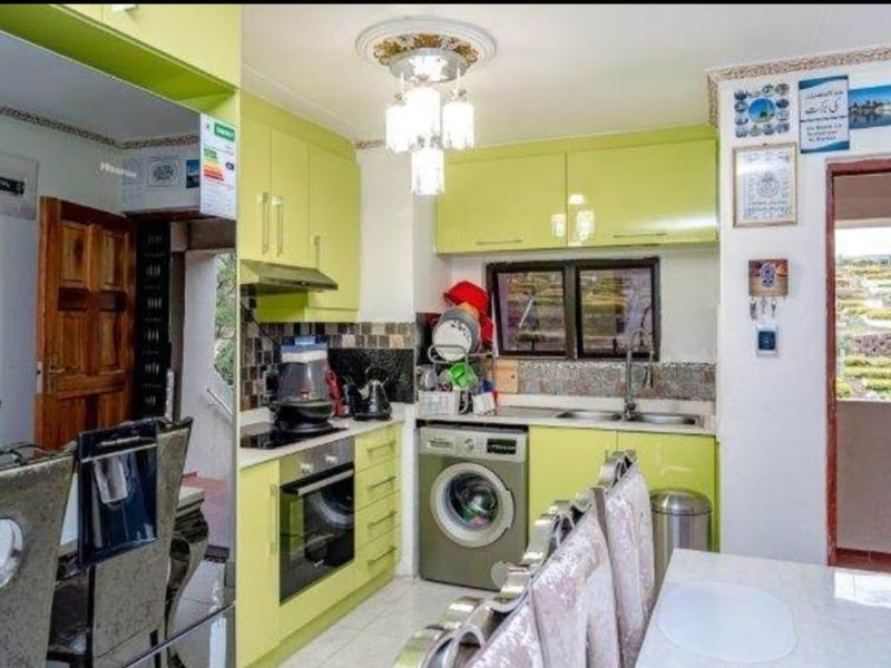 Compact kitchen featuring lime green cabinetry, built-in oven, hob, extractor fan, and integrated washing machine with a tiled backsplash and double sink.