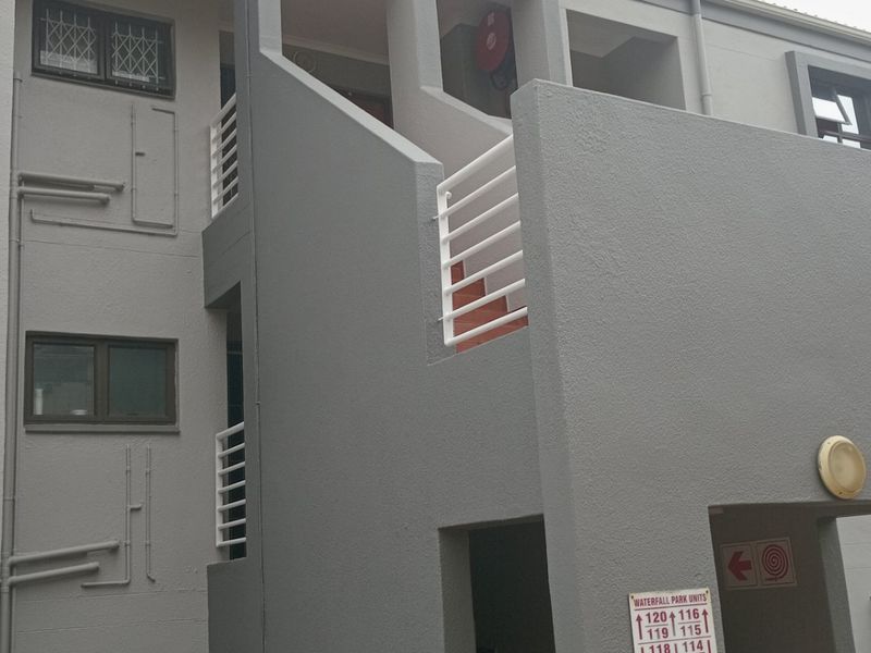 Exterior view of an apartment complex building featuring a concrete staircase, white railings, and grey textured facade.