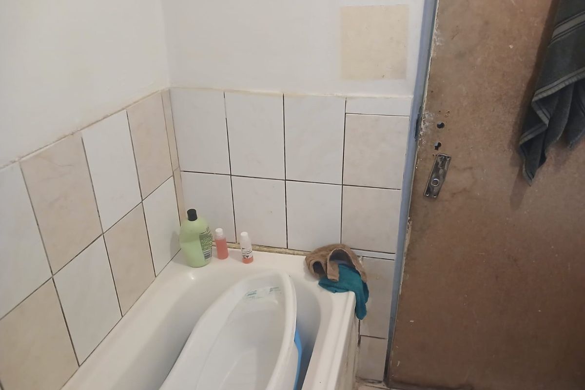 A small bathroom featuring a bathtub with tiled splashback and tiled flooring, requiring maintenance and cosmetic updates to the door and wall finishes.