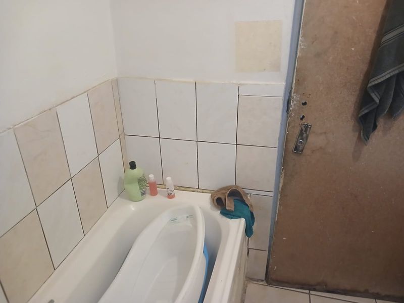 A small bathroom featuring a bathtub with tiled splashback and tiled flooring, requiring maintenance and cosmetic updates to the door and wall finishes.