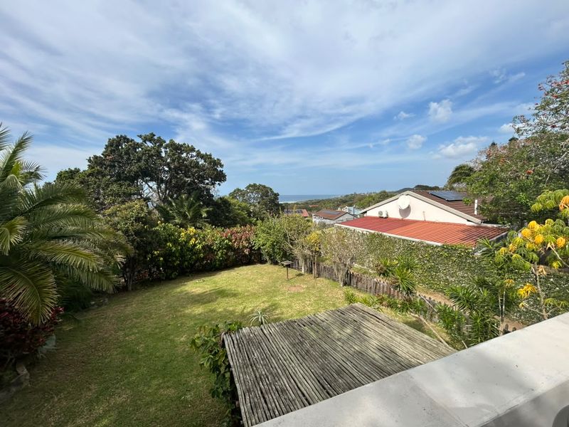 Elevated view overlooking a private garden with a timber pergola, mature landscaping, and distant ocean views.