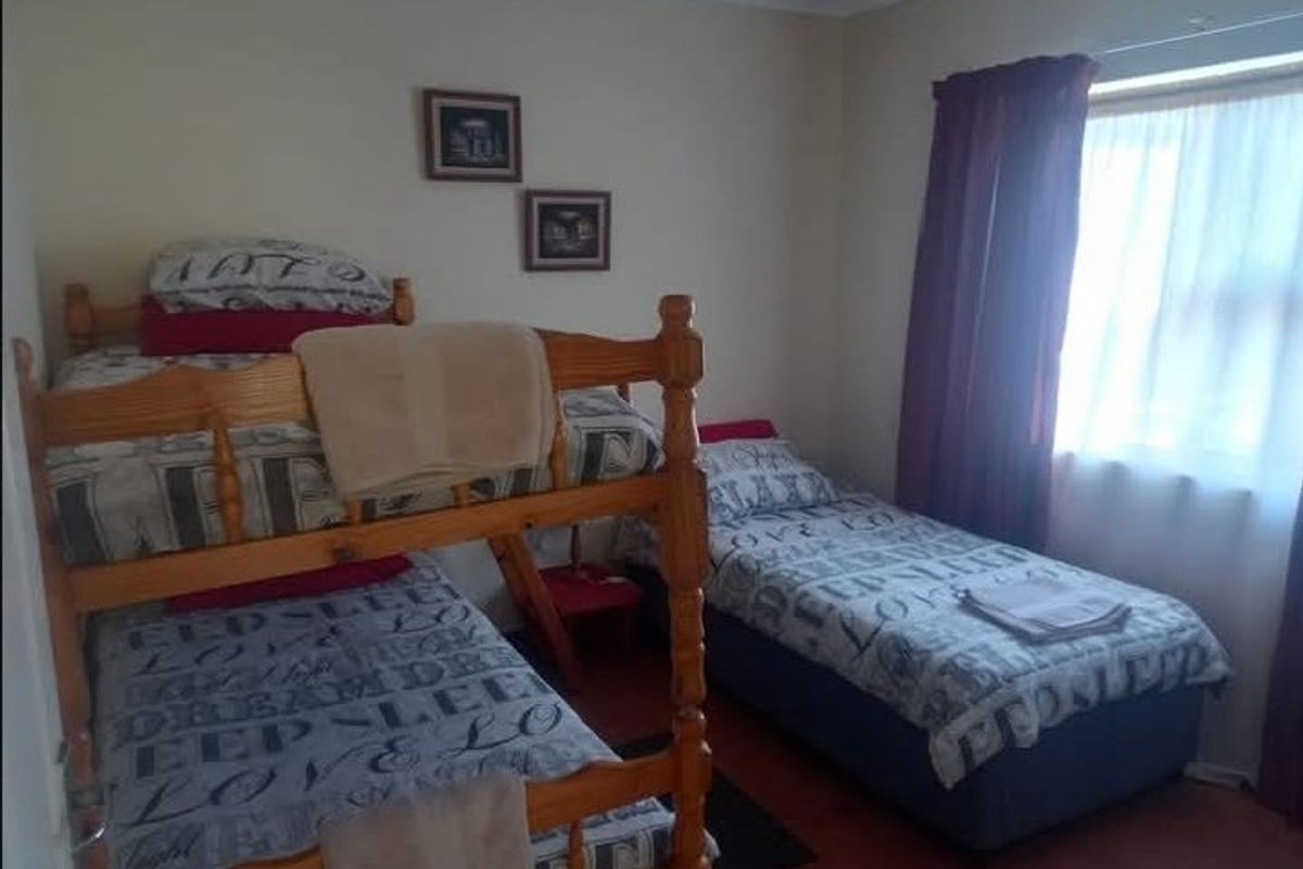 A functional bedroom featuring a window with curtain rails and tiled flooring, suitable for multiple occupants.