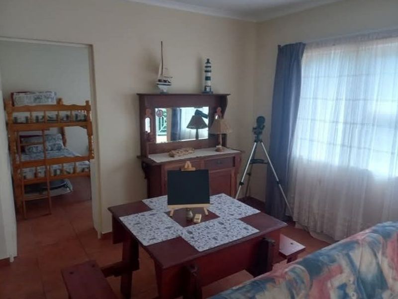 A living area featuring tiled flooring and natural light through a window, with an adjacent bedroom visible through the doorway.