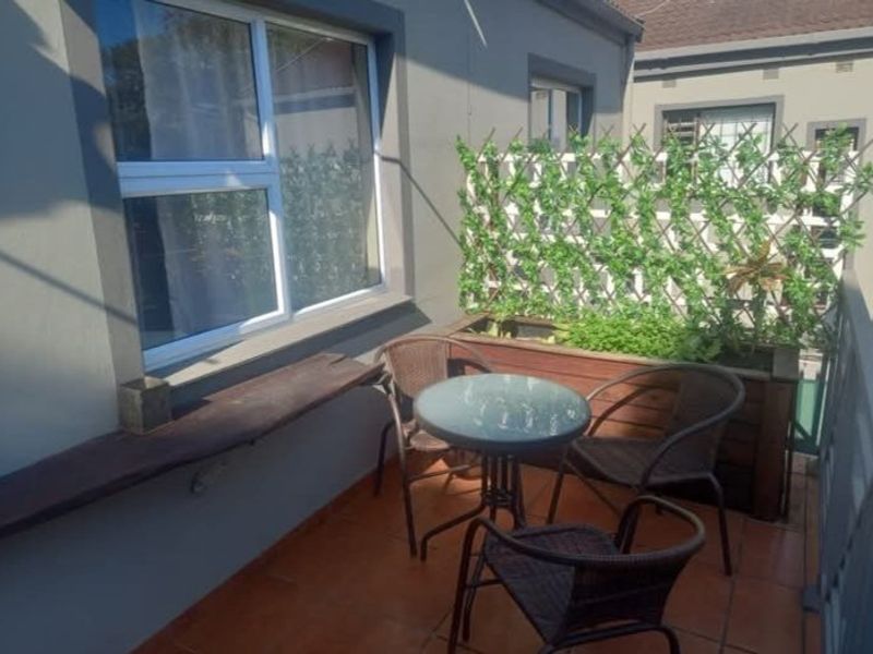 A compact balcony featuring tiled flooring, aluminium window frames, and a built-in wooden planter box with a trellis screen for added privacy.