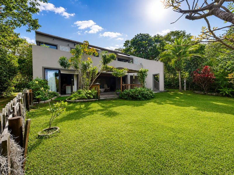 Rear view of the property featuring a spacious landscaped garden, a timber deck with a pergola, and large sliding glass doors.