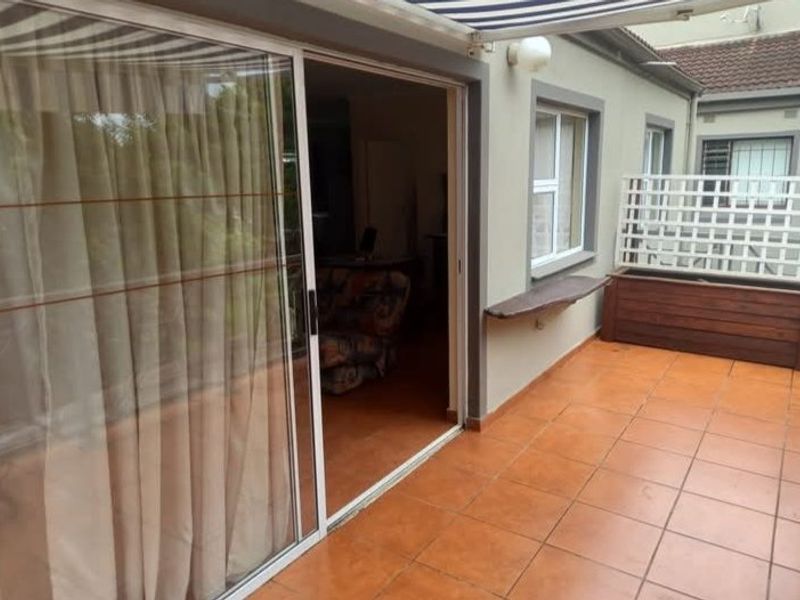Covered patio area featuring terracotta tiling, a retractable awning, and a built-in wooden planter box with a trellis screen.