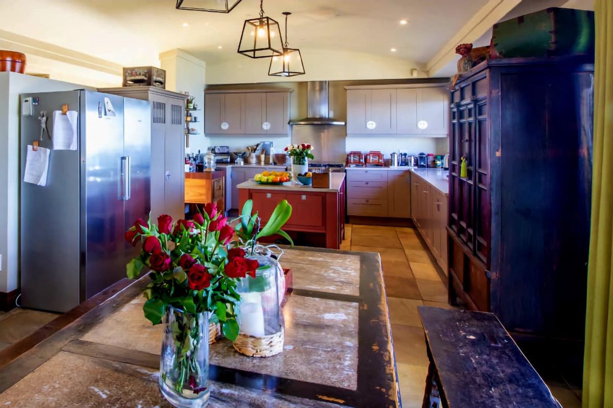 Spacious kitchen featuring built-in cabinetry, a central island, stainless steel extractor fan, and stone tile flooring, offering a functional and well-lit culinary space.