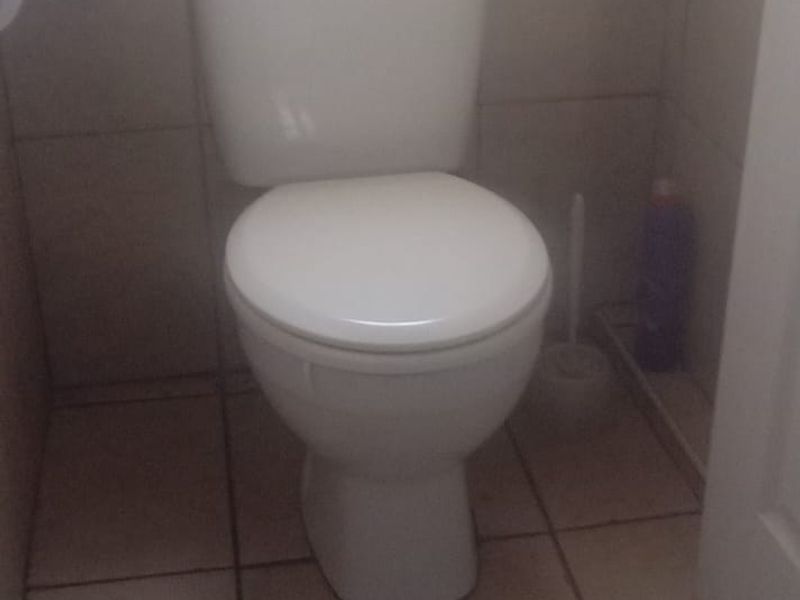 A compact bathroom featuring neutral ceramic floor and wall tiles with a standard white toilet suite.
