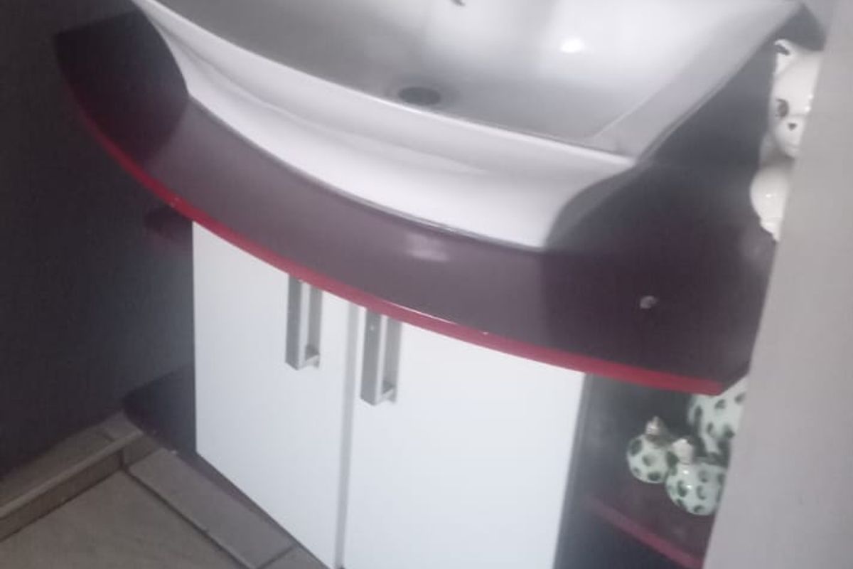 A compact bathroom vanity featuring a modern white ceramic basin, chrome mixer tap, and a two-tone cabinet with tiled flooring.