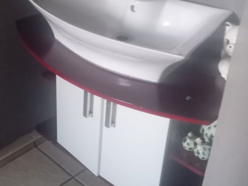 A compact bathroom vanity featuring a modern white ceramic basin, chrome mixer tap, and a two-tone cabinet with tiled flooring.