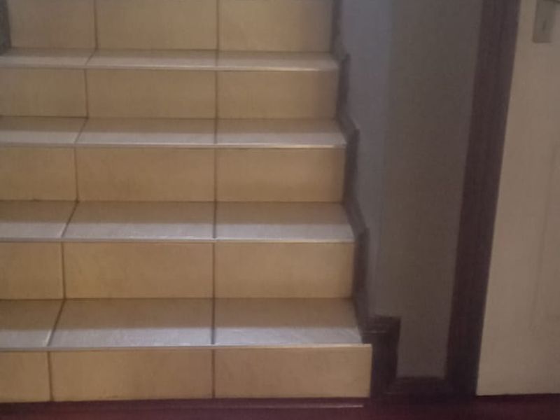 A staircase with tiled steps and a handrail, leading from a hallway with dark laminate flooring.