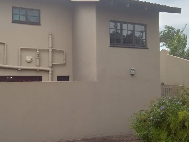 Front elevation of a townhouse featuring a boundary wall, exposed exterior plumbing, and casement windows.