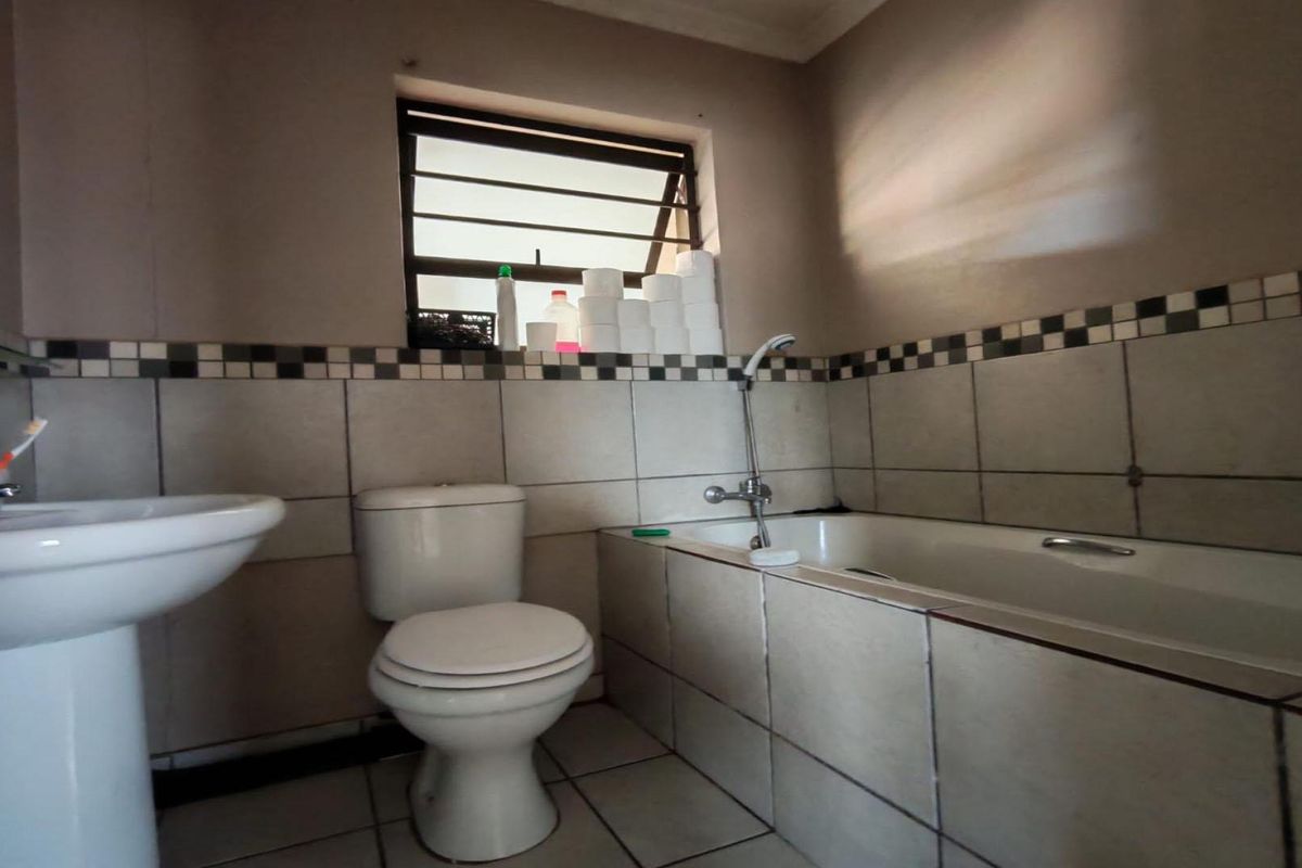 A functional bathroom featuring a pedestal basin, toilet, and bathtub with tiled walls and flooring, requiring cosmetic updates to modernize the space.