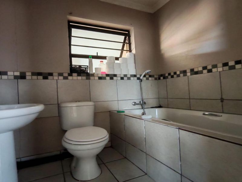 A functional bathroom featuring a pedestal basin, toilet, and bathtub with tiled walls and flooring, requiring cosmetic updates to modernize the space.