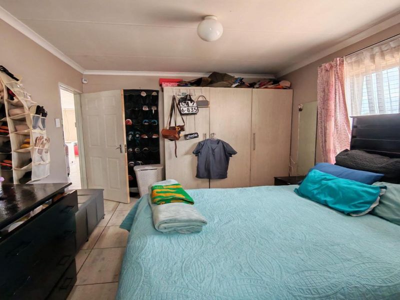 A functional bedroom featuring tiled flooring, a built-in wardrobe, and a window fitted with security bars.