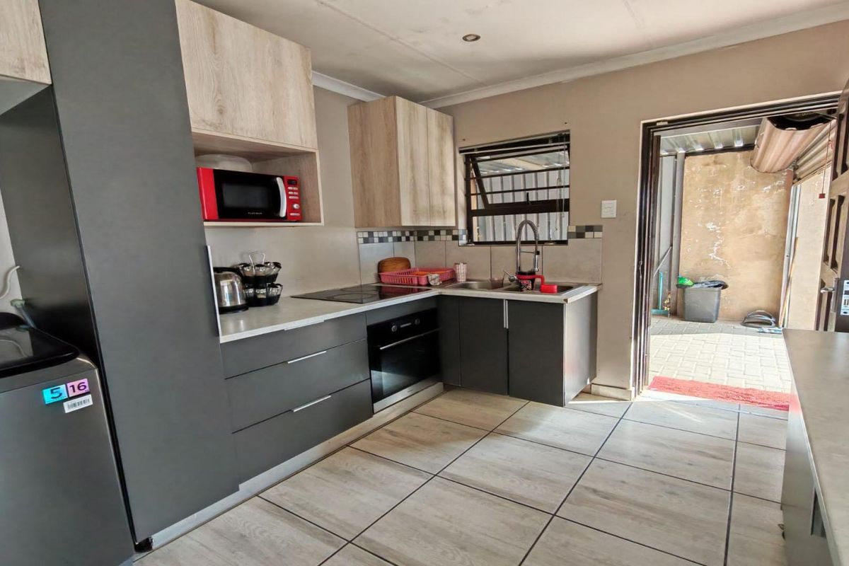 A compact kitchen featuring modern grey and wood-tone cabinetry, integrated oven and hob, tiled backsplash, and direct access to an outdoor area.