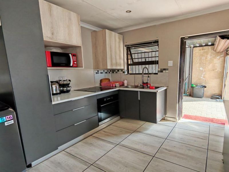A compact kitchen featuring modern grey and wood-tone cabinetry, integrated oven and hob, tiled backsplash, and direct access to an outdoor area.