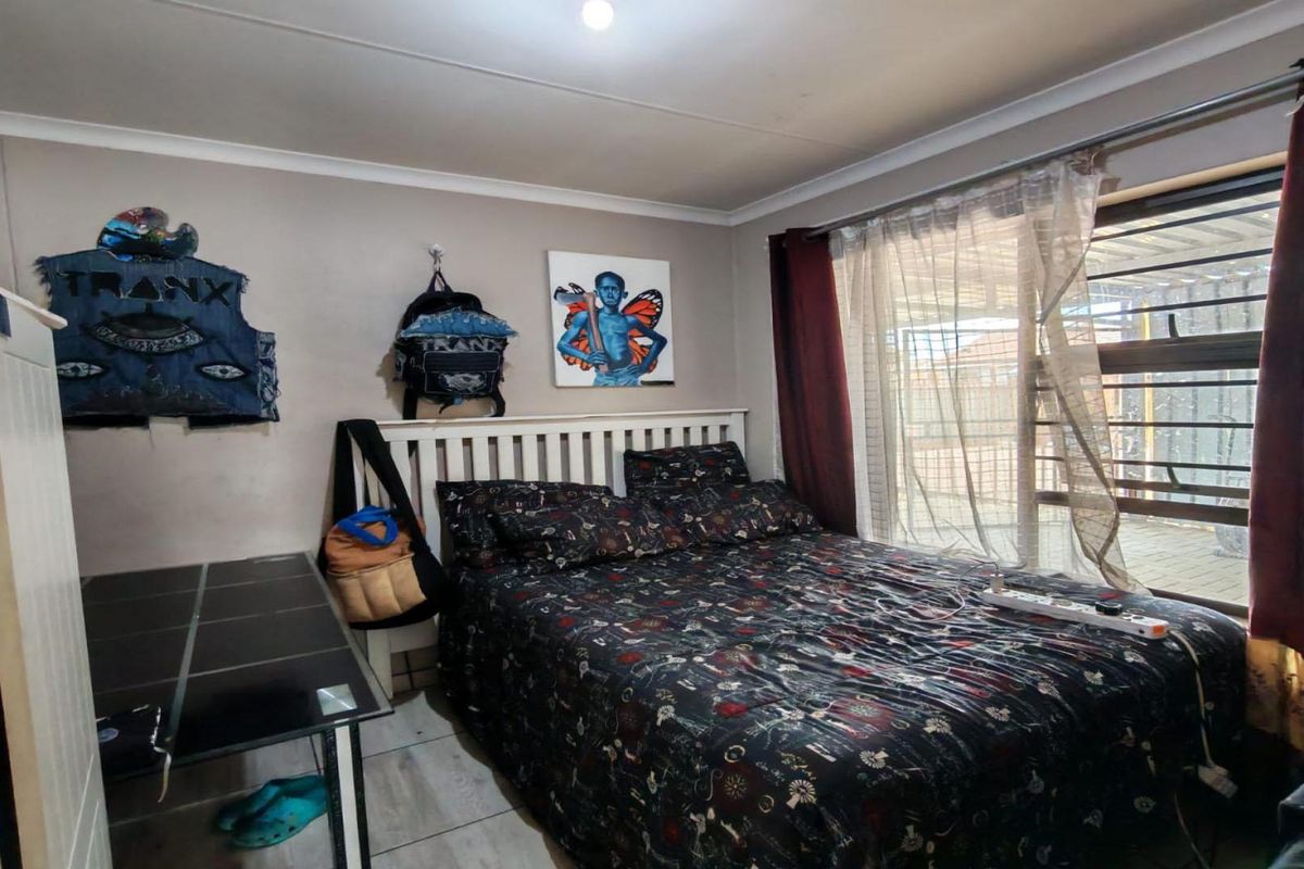 A functional bedroom featuring tiled flooring, a large window with security bars, and neutral wall finishes.