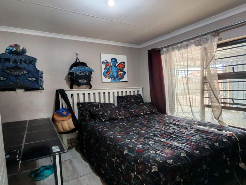 A functional bedroom featuring tiled flooring, a large window with security bars, and neutral wall finishes.