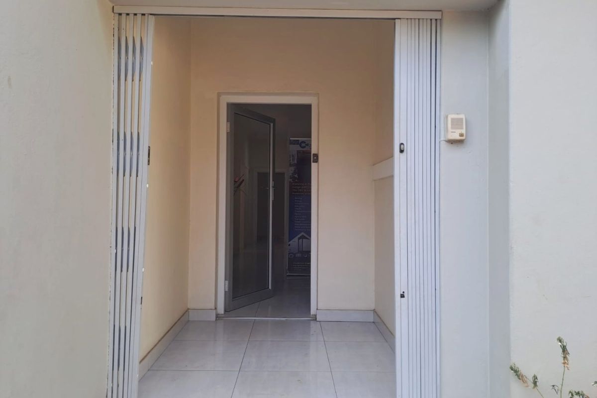 A secure commercial entrance featuring a retractable security gate, tiled flooring, and an intercom system leading into the main building interior.