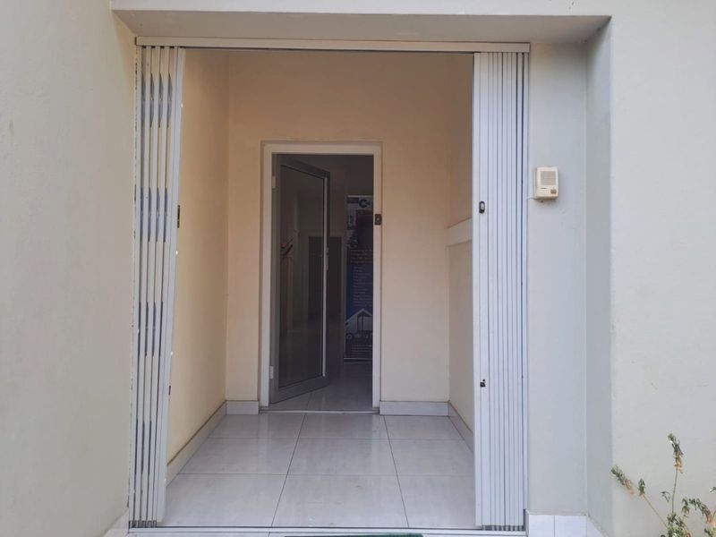 A secure commercial entrance featuring a retractable security gate, tiled flooring, and an intercom system leading into the main building interior.