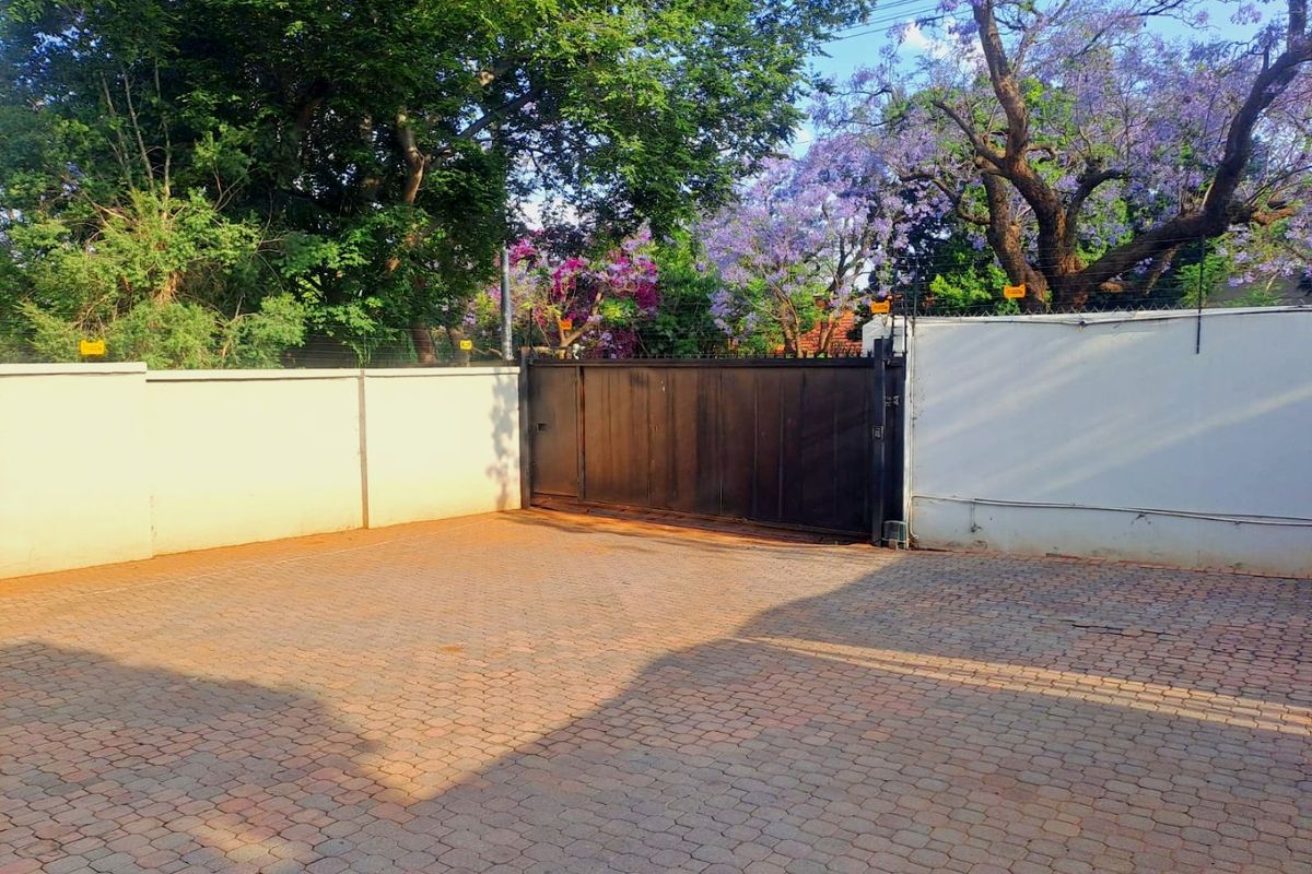 A secure commercial property entrance featuring a paved driveway, perimeter wall with electric fencing, and a sliding metal gate.