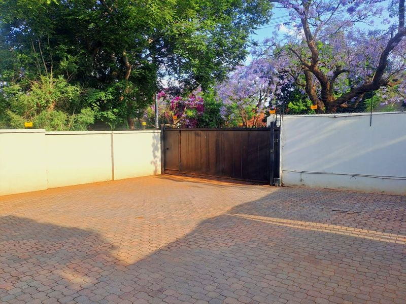 A secure commercial property entrance featuring a paved driveway, perimeter wall with electric fencing, and a sliding metal gate.