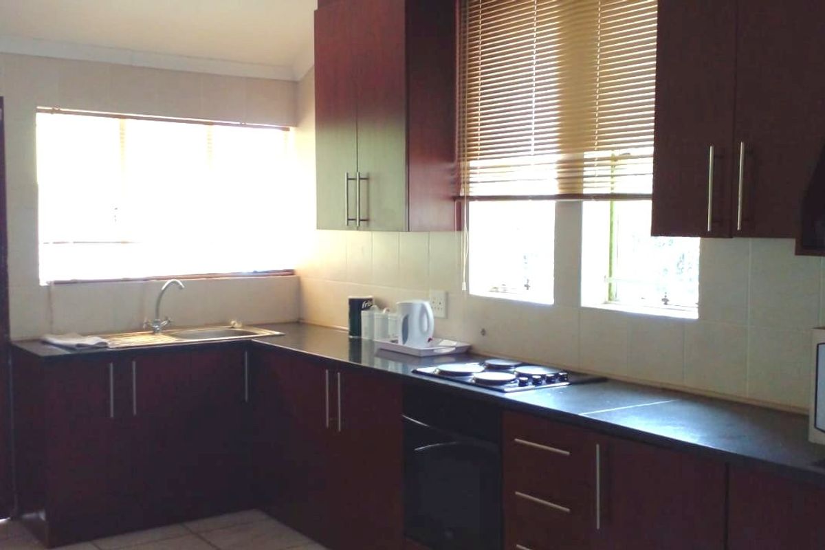 A functional kitchen featuring dark wood cabinetry, granite countertops, a built-in hob and oven, and tiled backsplash with natural light from windows.