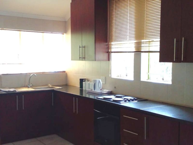 A functional kitchen featuring dark wood cabinetry, granite countertops, a built-in hob and oven, and tiled backsplash with natural light from windows.