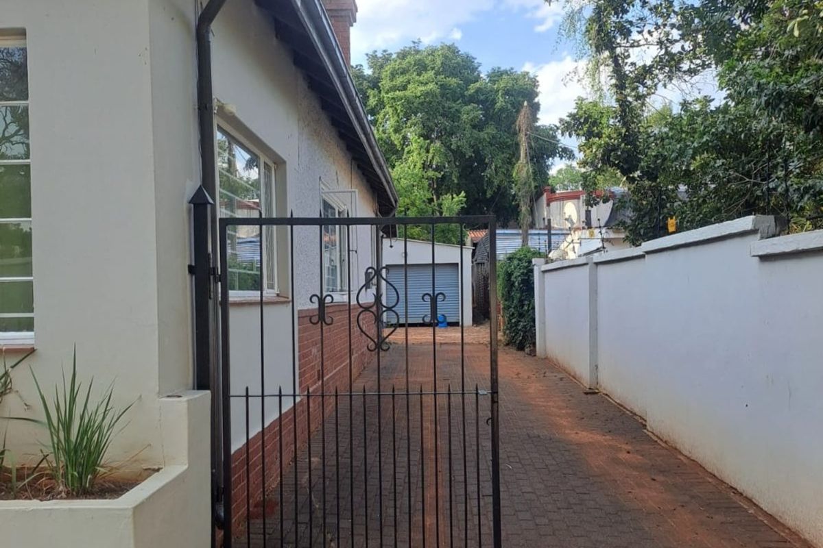 A side access path featuring a wrought iron gate, paved driveway, and boundary wall leading towards a detached garage at the rear of the property.