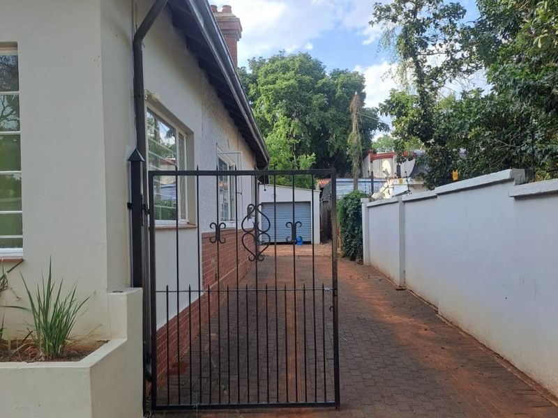 A side access path featuring a wrought iron gate, paved driveway, and boundary wall leading towards a detached garage at the rear of the property.