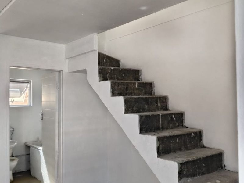 An unfinished interior hallway featuring a concrete staircase and access to an adjacent bathroom, currently in a shell condition awaiting final finishes.