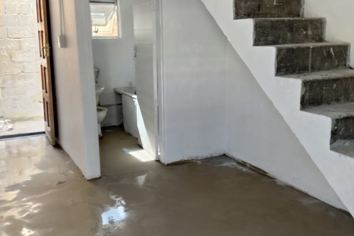An unfinished interior space featuring a raw concrete staircase, polished concrete flooring, and direct access to an adjoining bathroom area.