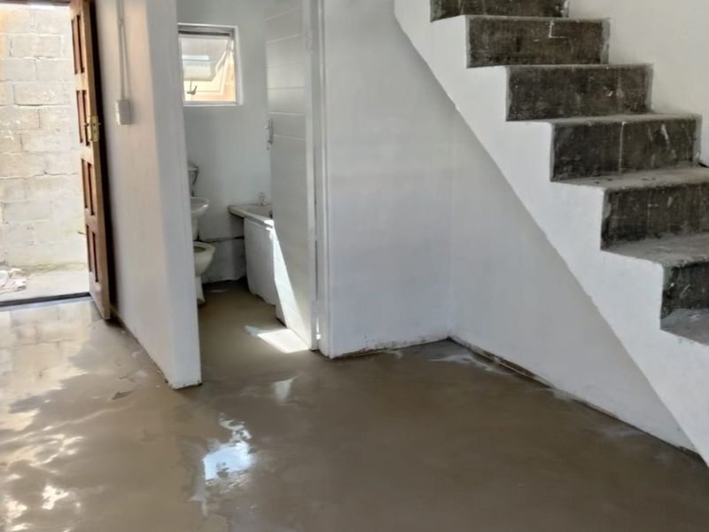 An unfinished interior space featuring a raw concrete staircase, polished concrete flooring, and direct access to an adjoining bathroom area.