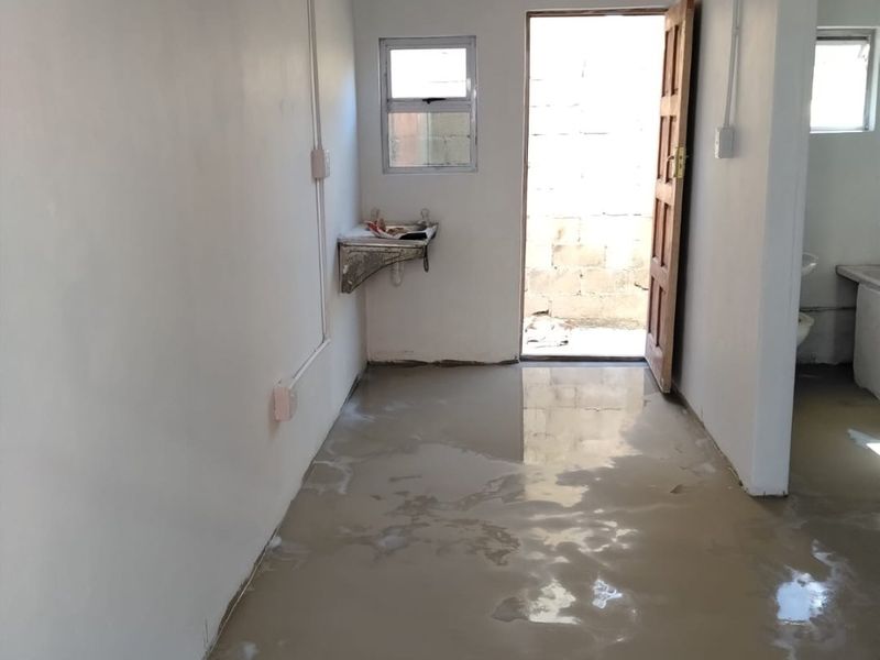 An unfinished utility space featuring exposed electrical conduit, a wall-mounted basin, and direct access to an outdoor area.