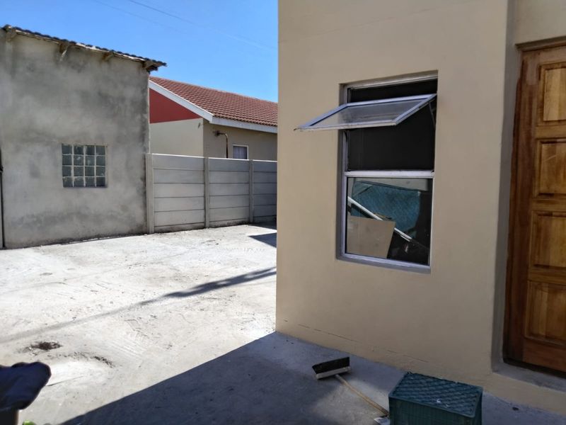 Rear exterior view showing a paved yard area, precast concrete boundary wall, and the side elevation of the main dwelling with a timber door.