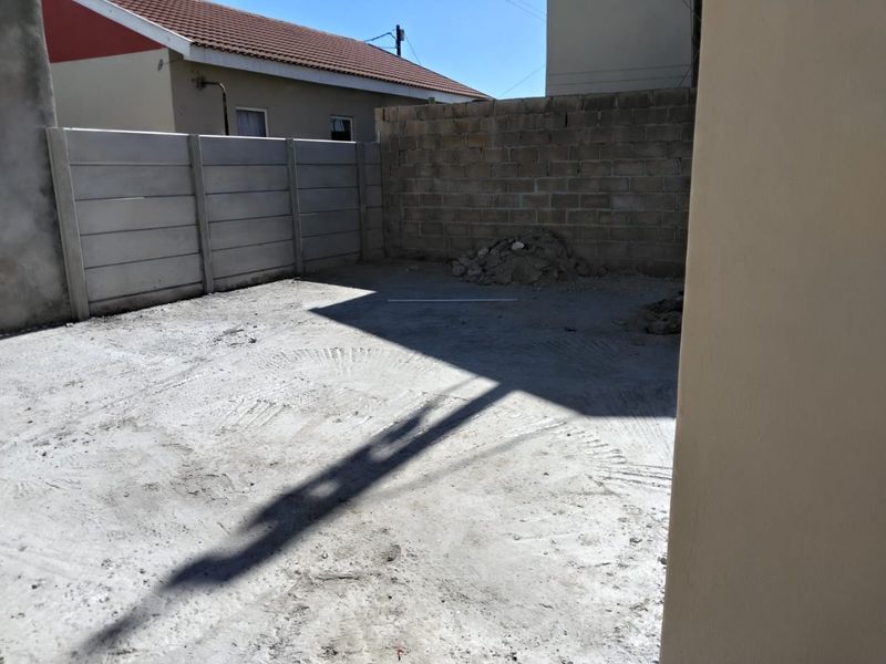 An unfinished rear yard area featuring a concrete slab, enclosed by precast concrete and block boundary walls.