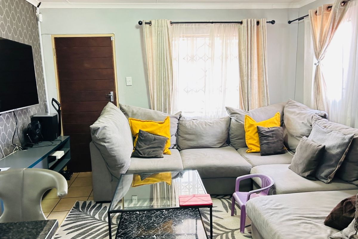 A comfortable living room featuring tiled flooring, a timber entrance door, and security gate, providing a functional and well-lit space for relaxation.