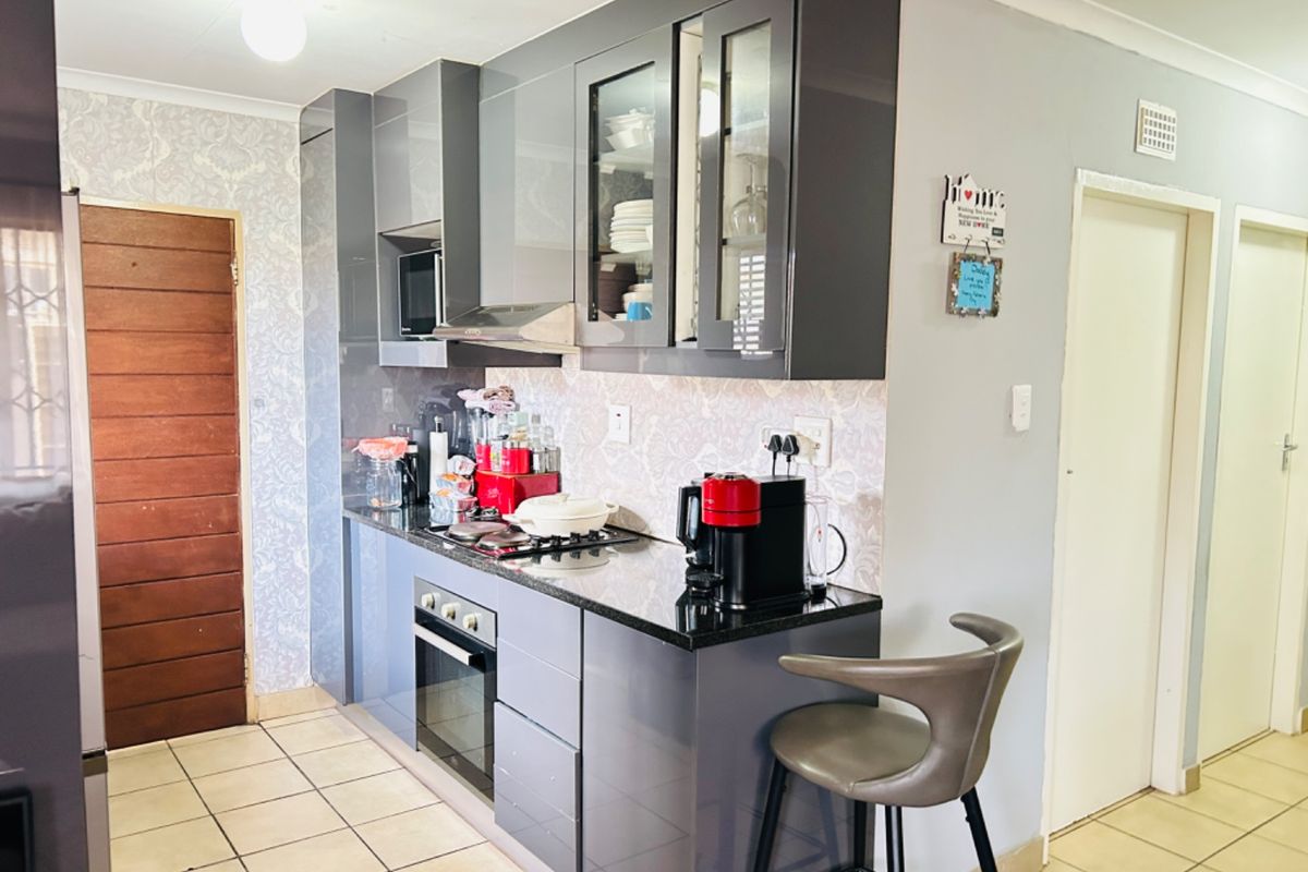 Modern kitchen featuring sleek grey cabinetry, granite countertops, built-in oven, gas hob, and extractor fan, complemented by tiled flooring.