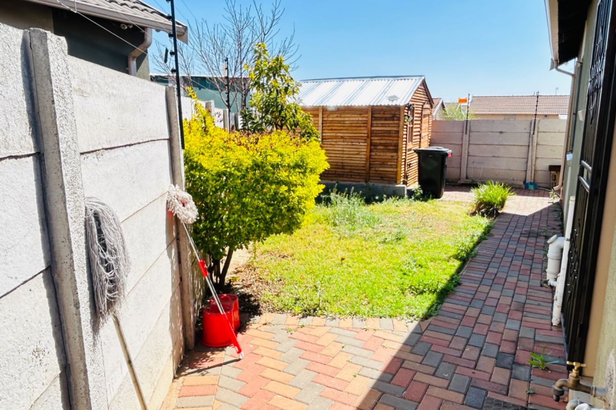 A rear garden area featuring a paved walkway, precast concrete boundary walls with electric fencing, and a wooden storage shed.