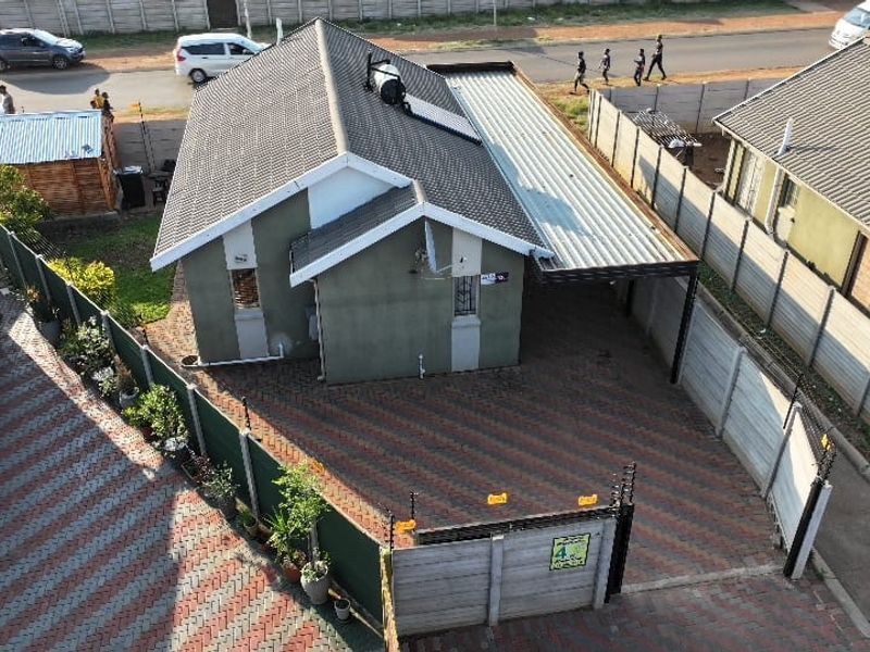 Aerial view of a residential property featuring a tiled roof with solar geyser, paved driveway, carport, and secure perimeter walling with electric fencing.