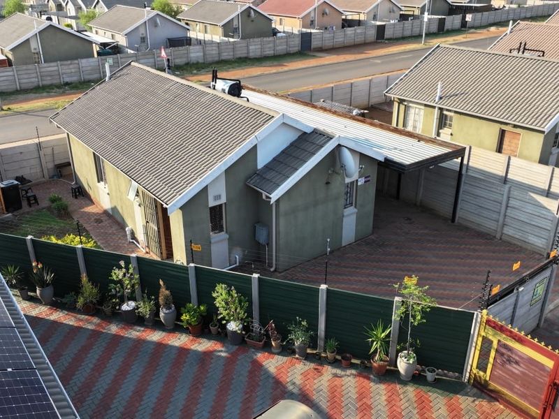 Aerial view of a residential property featuring a tiled roof, paved driveway, carport, and secure perimeter wall with electric fencing.